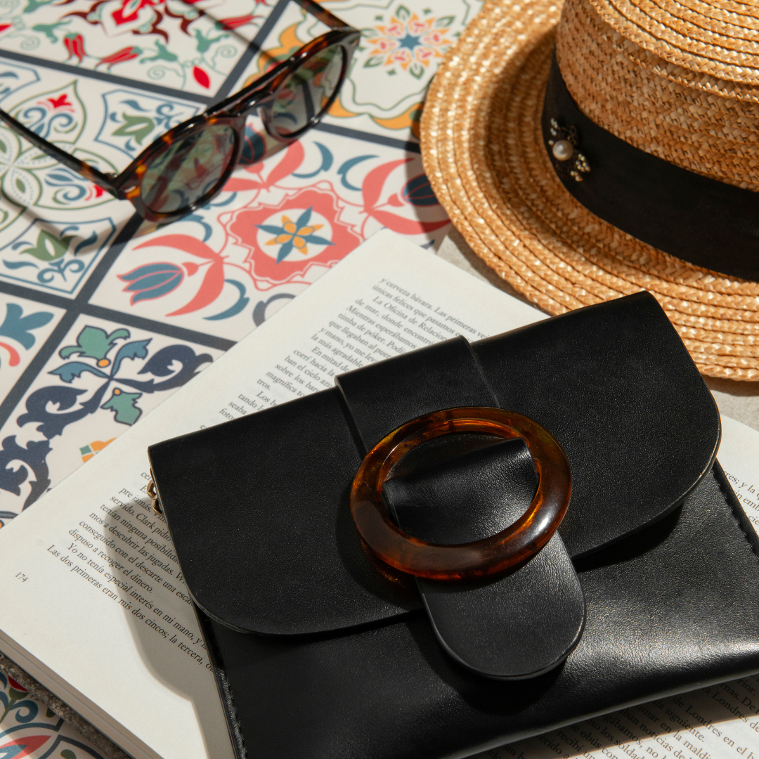 Women's fashion accessories flatlay with black handbag sunglasses and straw hat — Emmie & Ellie accessories